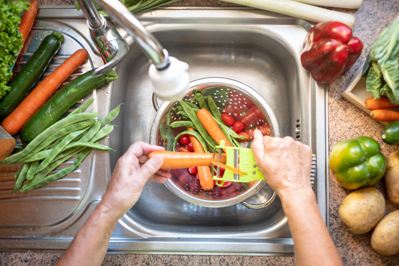 person washes vegetables in a kitchen sink